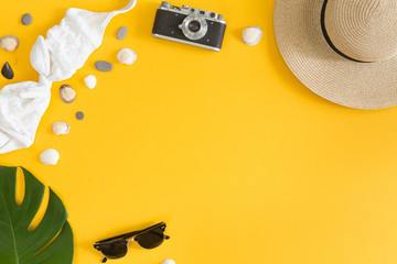 Top view of traveler outfit on yellow background with copy space, flat lay summer and travel concept. Swimsuit, photo camera, hat and green tropical palm leaf