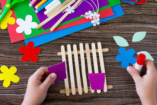 The child glues the details of the gift of summer flowers on wooden sticks fence. Handmade. Project of children's creativity, handicrafts, crafts for kids.
