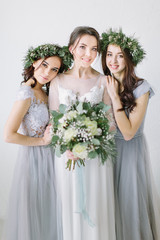 Beautiful laughing bride in a white wedding dress holding bouquet with bridesmaids in blue grey dresses and wreathes