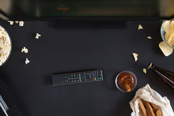 Popcorn, snack and a remote control for the TV, top view and flat lay on black background