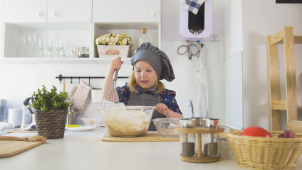 Little girl mixes the mixture for cookies with a big spoon