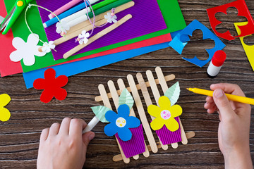A child is drawing a gift of summer flowers on a wooden sticks fence. Handmade. Project of children's creativity, handicrafts, crafts for kids.