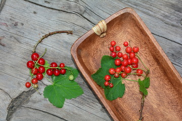Rote Johannisbeeren in Holzschale und auf rustikalem Holz  mit grünen Blättern