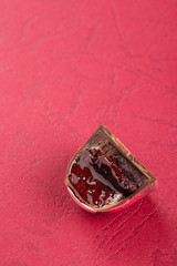 Cut handmade candy with chocolate ganache and cherry confiture filling on red background