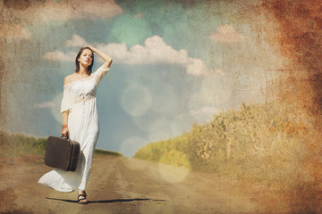 Fototapeta na wymiar photo of beautiful young woman holding suitcase and standing on the road on the wonderful sky background