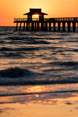 Naples, Florida yellow and orange sunset vertical view in gulf of Mexico with sun setting inside Pier wooden jetty, horizon and dark blue ocean waves