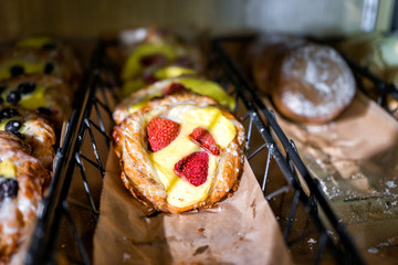 Closeup of many yellow cream cheese berry fruit strawberry baked danish pastries on shelf tray display desserts in bakery shop cafe store rustic