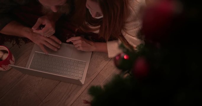 Redhead couple using laptop for online shopping under Christmas tree