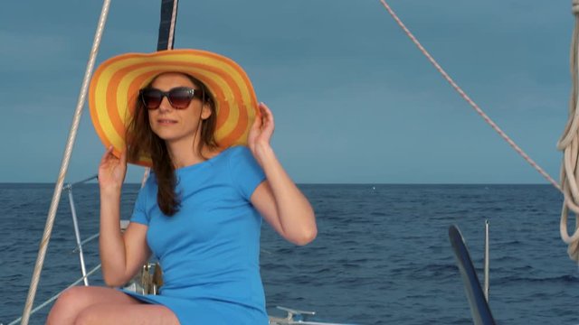 Woman in a yellow hat and blue dress waving hair and smiling on yacht on summer season at ocean