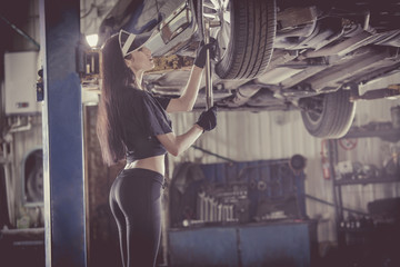 Woman mechanic is repairing a car on the lift.