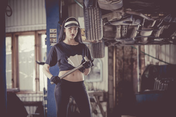 Woman mechanic is holding a cylinder key in front of the car on the lift