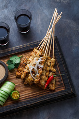 Close view of malaysian chicken skewers - satay or sate ayam with peanut sauce, dark background
