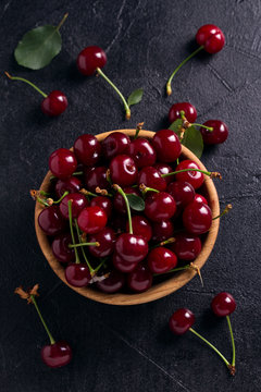 Fresh cherry in wooden bowl on black background. Fresh ripe sweet cherries. View from above, top studio shot
