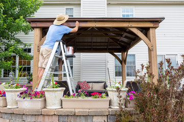 Man staining a backyard gazebo behind his house