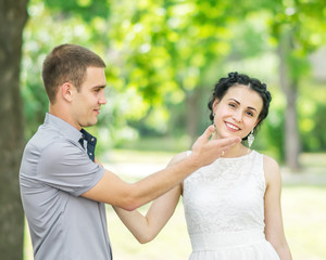 Portrait of male bridegroom touching face of beautiful young female bride in summer park. Couple in love. Emotions and gestures