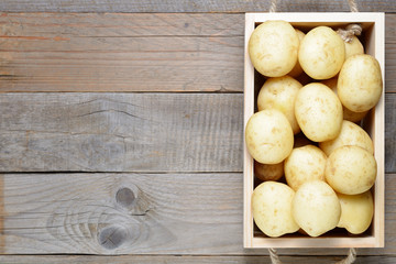 Raw potatoes in box on wooden table