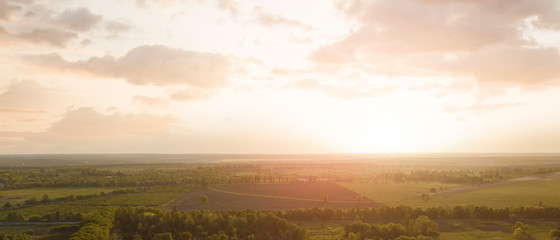 Aerial view from the drone, a bird's eye view of abstract geometric forms of agricultural fields with a dirt road through them in the summer evening at sunset.