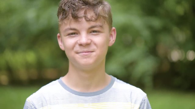 Close up emotional portrait of caucasian smiling teen boy. Handsome guy. Funny cute teenager in summer park at day. Child looking at camera.