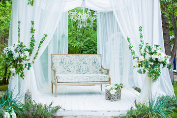 Wonderful summer white gazebo with white curtains, and luxurious sofa on background park