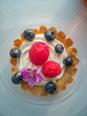 Delicious cream tart with berries and edible flower on top.