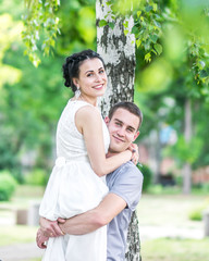 Fototapeta premium Portrait of young couple female bride and male bridegroom hugging in summer park. Man husband raised woman wife and both looking into camera. Couple in love under birch tree. Happy family smiling