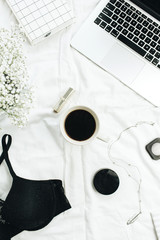 Female fashion blog concept with laptop, bra, coffee, flowers, cosmetics and accessories on white linen. Home working composition.