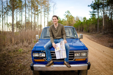 Man sitting on blue truck hood with map on dirt road