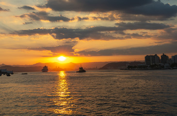 Obraz premium Cargo ship leaving the harbor, sailing out to sea with a beautiful sunset 