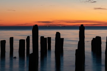 Silhouettes of a ruined pier, late sunset, night, two ships on the horizon, stratus clouds, long exposure