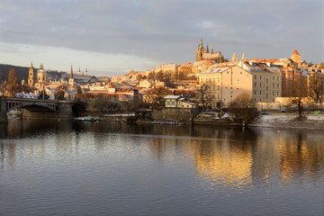 Fototapeta premium Sunny snowy early morning Prague Lesser Town with gothic Castle above River Vltava, Czech republic