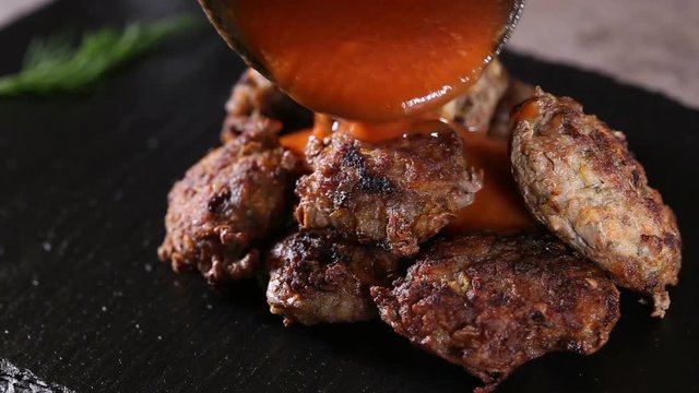 Pouring tomato marinated sauce over pork and beef meatballs 