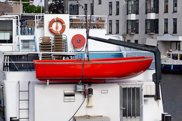 Red lifeboat hanging on the crane of the ship docked in the marina