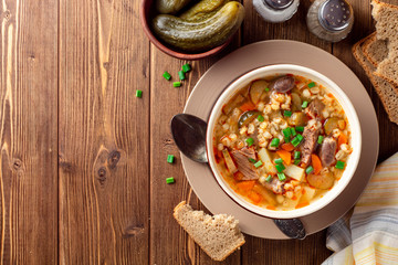 Traditional Russian soup Rassolnik with pickled cucumbers and pearl barley in bowl on wooden table