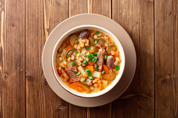 Traditional Russian soup Rassolnik with pickled cucumbers and pearl barley in bowl on wooden table