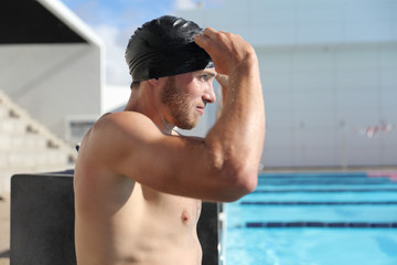 Swimming pool sport male athlete putting on cap and goggles getting ready for swim training at stadium swimmer center. Man exercising at fitness gym.