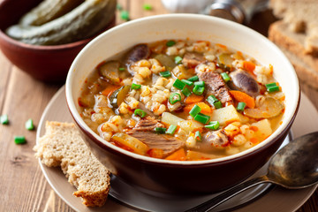 Traditional Russian soup Rassolnik with pickled cucumbers and pearl barley in bowl on wooden table