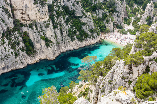 View from above of the calanque of En-Vau, a hard-to-reach narrow natural creek with white sandy beach close to Marseille and Cassis, with people sunbathing and swimming in the crystal clear water.