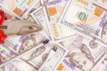 Tools lying over 100 dollars banknotes background. Pliers and screwdriver against US money. Correction, adjustment and improvement of budget and finance concept. Toned. Copyspace
