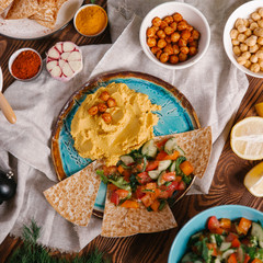Top view of plate with hummus served with different kinds on vegetables and pita