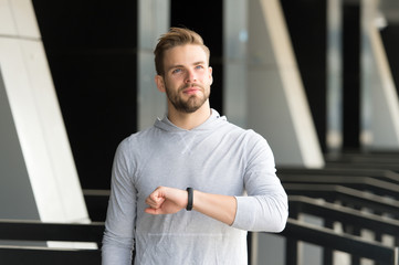 Man athlete on satisfied face checking time, urban background. Athlete with bristle with fitness tracker or pedometer finished on time. Sportsman training with pedometer gadget. Just on time concept