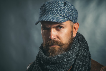 Male fashion. Handsome man in hat and scarf. Winter fashion. Attractive bearded man in warm knitted hat and scarf. Serious man wearing demi-season clothing. Copy space for advertise clothing store.