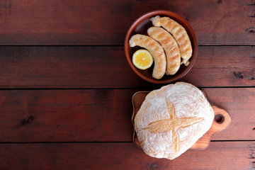 Sausages cooked on a grill on a dark wooden background, chicken sausages on a clay bowl, bread in flour sintered in a stove, meat dish and rustic bread, copy space