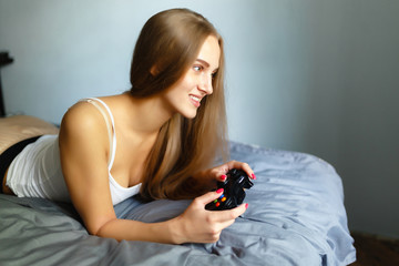 Girl gamer plays with a wireless gamepad while looking at the screen in front of her. Young blonde...