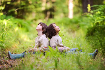 Two boys in identical sweaters sitting on a forest road