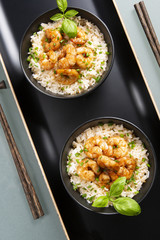 Two bowls of black color with rice and fried shrimp on a blue table. Asian food.