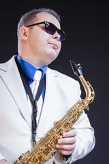 Fototapeta na wymiar Dreaming Male Saxophonist Posing In Sunglasses With Sax. Against Black Background