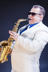 Music Concepts. Expressive Mature Playing Saxophonist Posing In Sunglasses With Sax. Against Black...