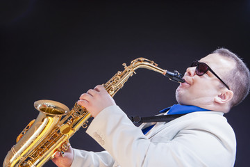 Music Concepts. Expressive Mature Playing Saxophonist Posing In Sunglasses With Sax. Against Black Background.