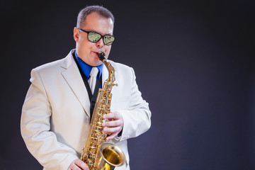 Fototapeta premium Music Concepts. Portrait of Caucasian Mature Male Saxophone Player Posing In Sunglasses With Musical Notes Reflections With Sax. Against Black Background.