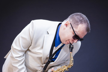 Music Concepts. Portrait of Expressive Playing  Mature Male Saxophonist Posing In Sunglasses With Sax. Against Black Background.